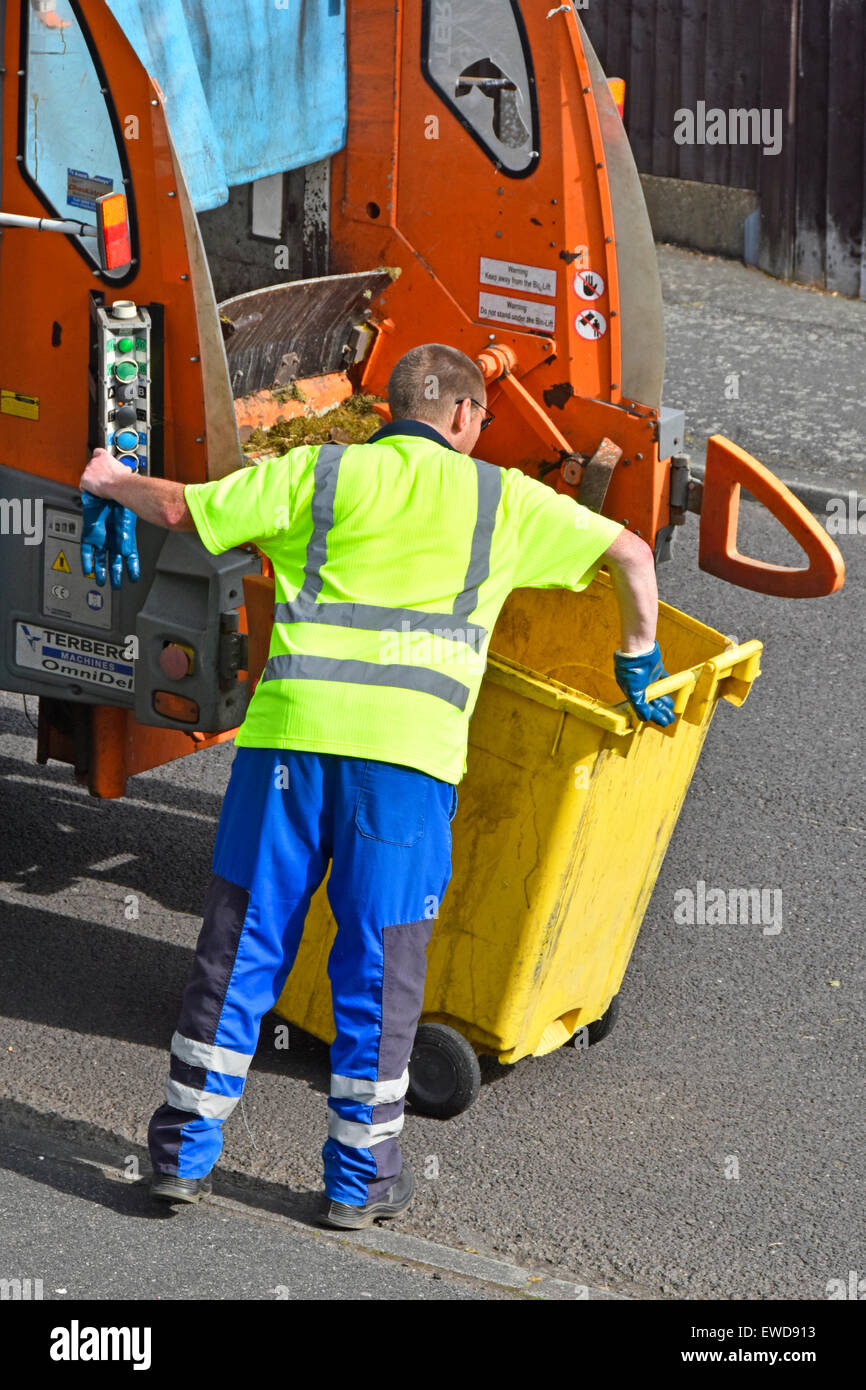 Refuse collector working lifting controls for wheelie bin back view of bin lorry collecting household rubbish in residential street Essex England UK Stock Photo