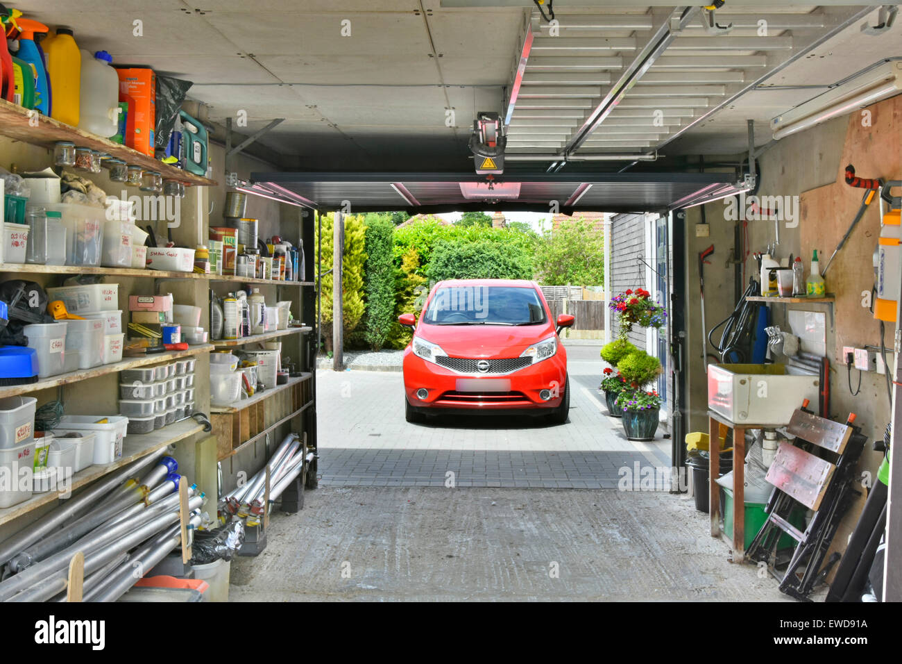 Car on driveway from inside a garage attached to house used for car parking & household storage of paraphernalia tools & garden sundries Essex England Stock Photo