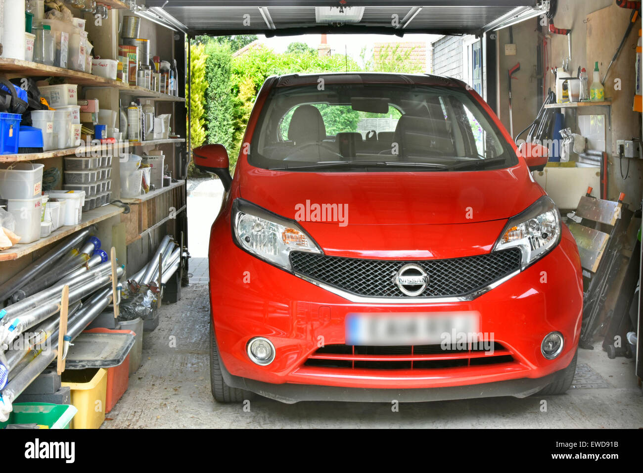Vehicle in garage attached to residential property red Nissan car parked shelving storage of sundry household paraphernalia & tools Essex England UK Stock Photo