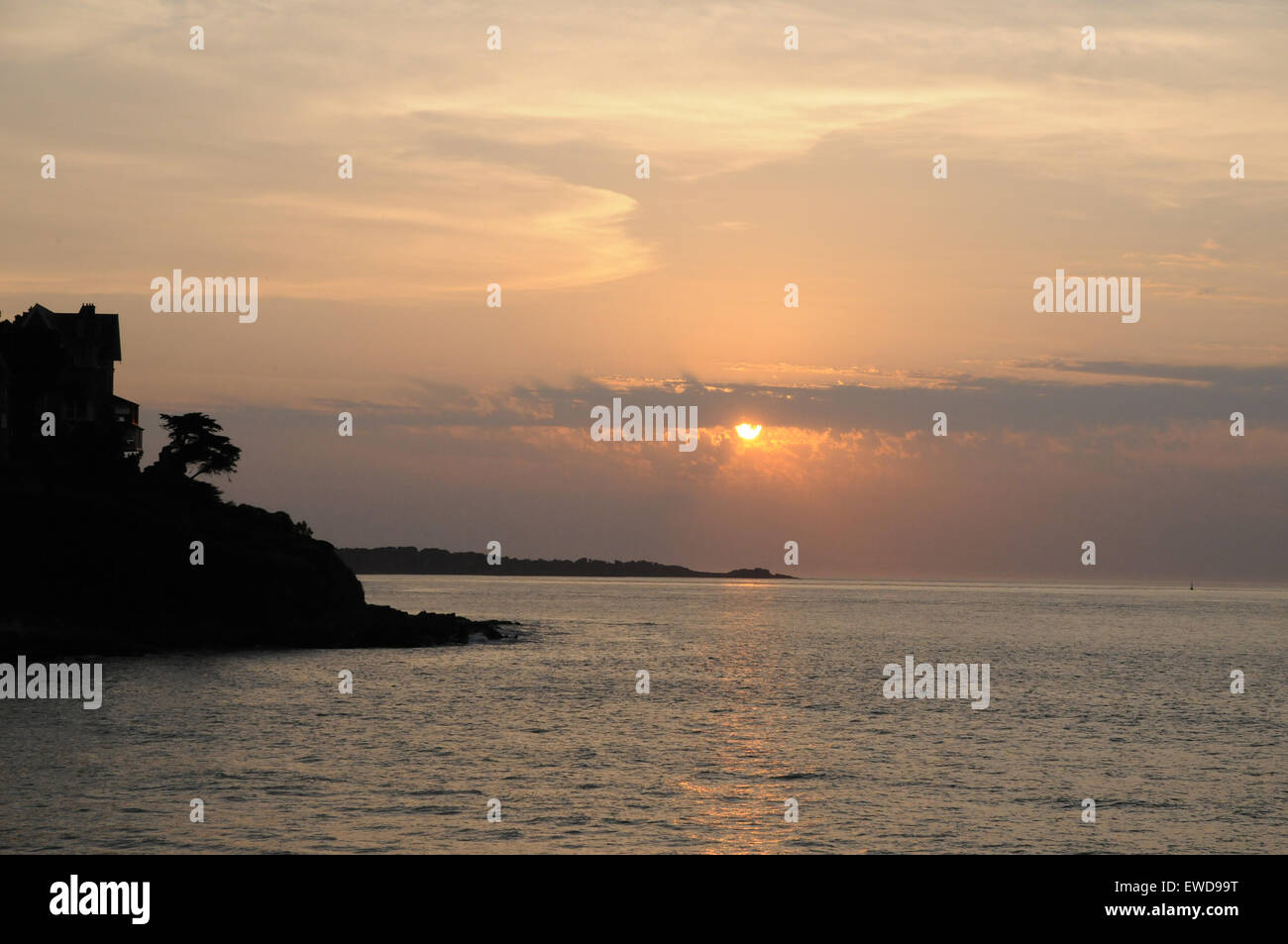The setting sun over the Granit Rose (pink granite) coast of Brittany as seen from the beach at Trestrignel near Perros Guirec. Stock Photo