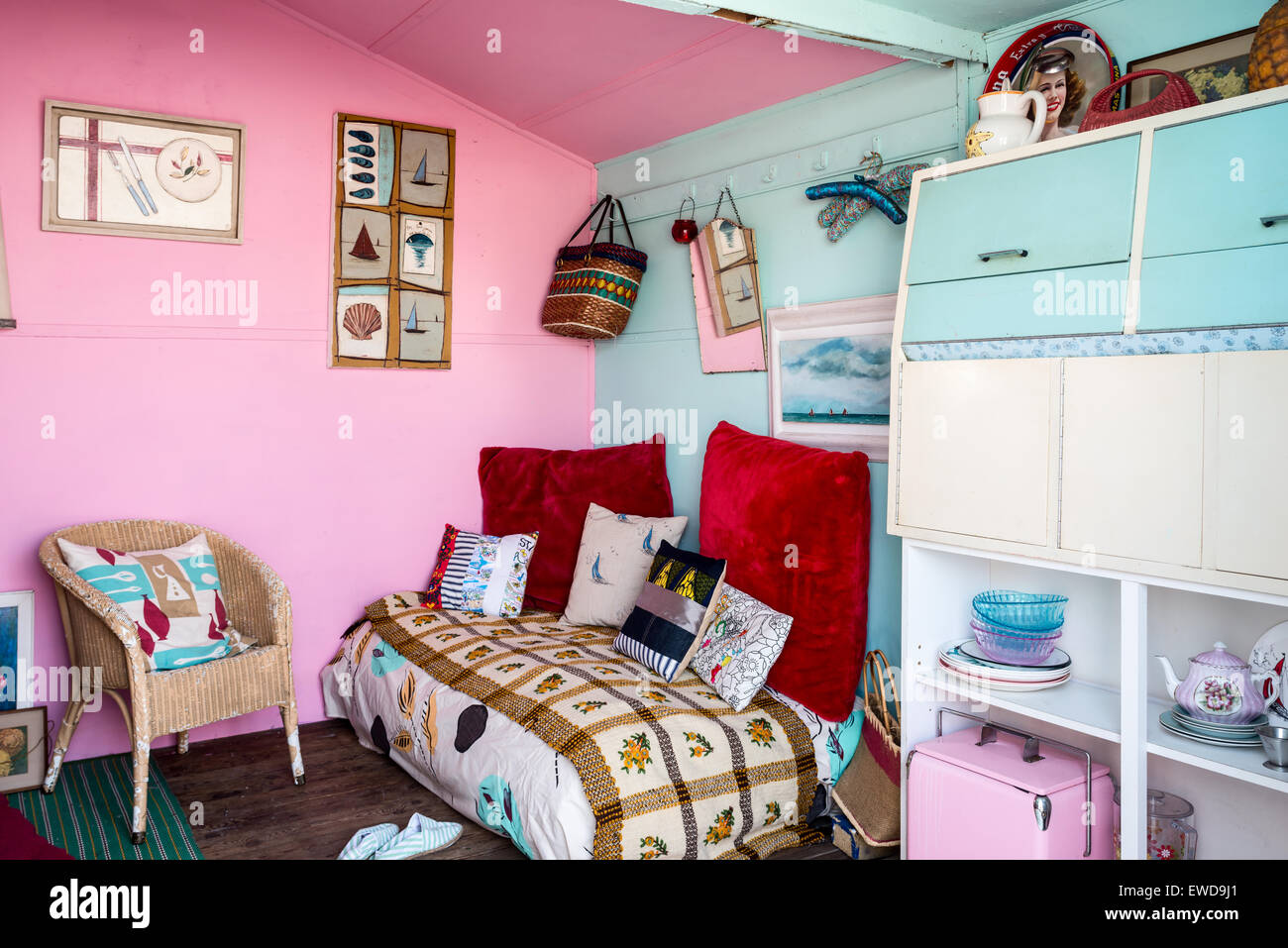 Seconda Vita cushions on daybed in seating area with pink and blue walls, wicker armchair and nautical artwork Stock Photo