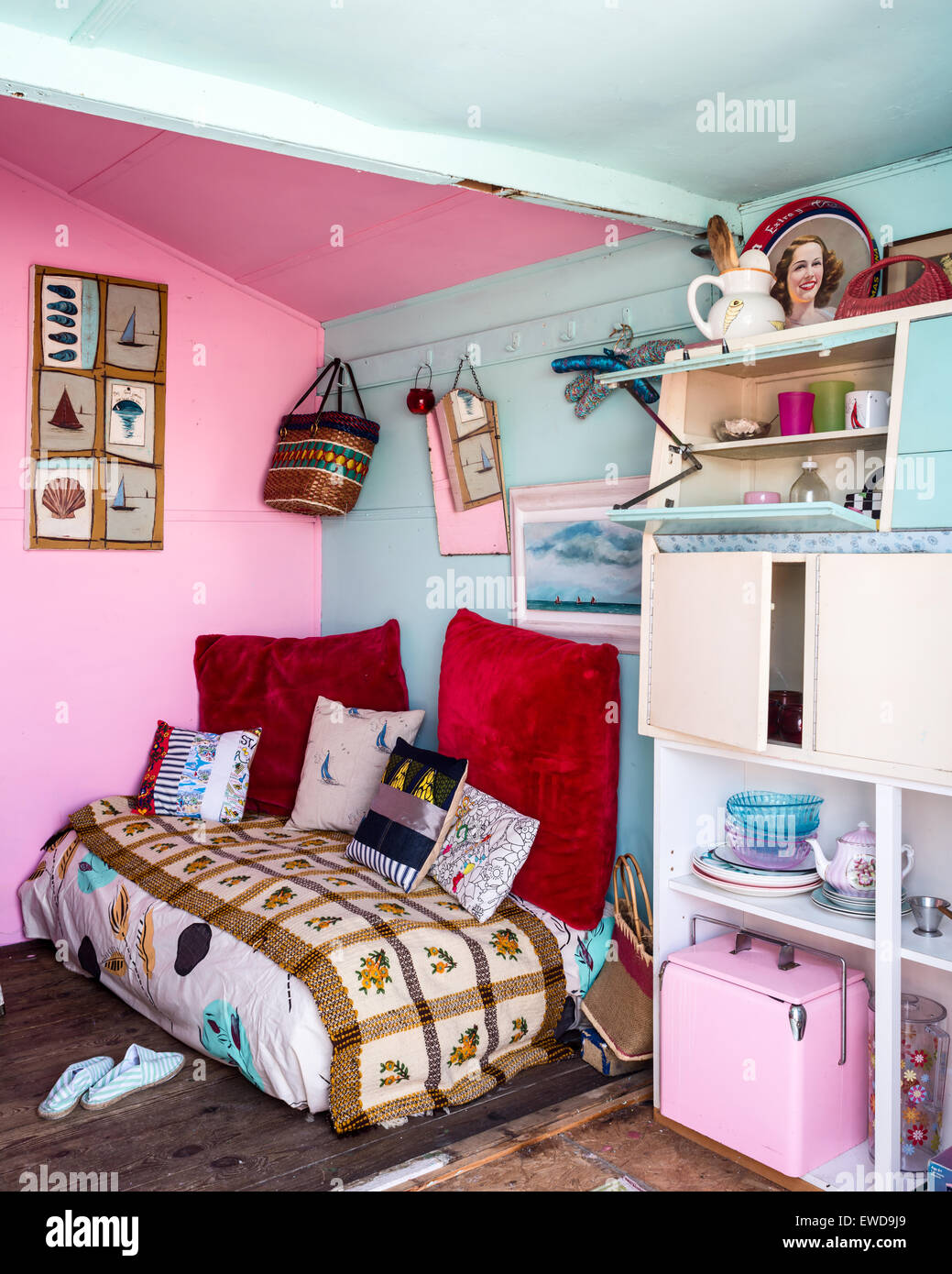 Seconda Vita cushions on daybed in seating area with pink and blue walls, wicker armchair and nautical artwork Stock Photo
