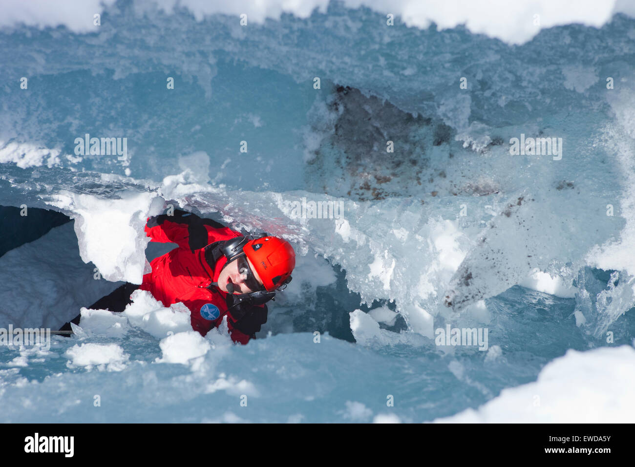 A mountain rescue paramedic is far down in a glacier crevasse looking up to the surface. In winter the mountain rescue service Stock Photo