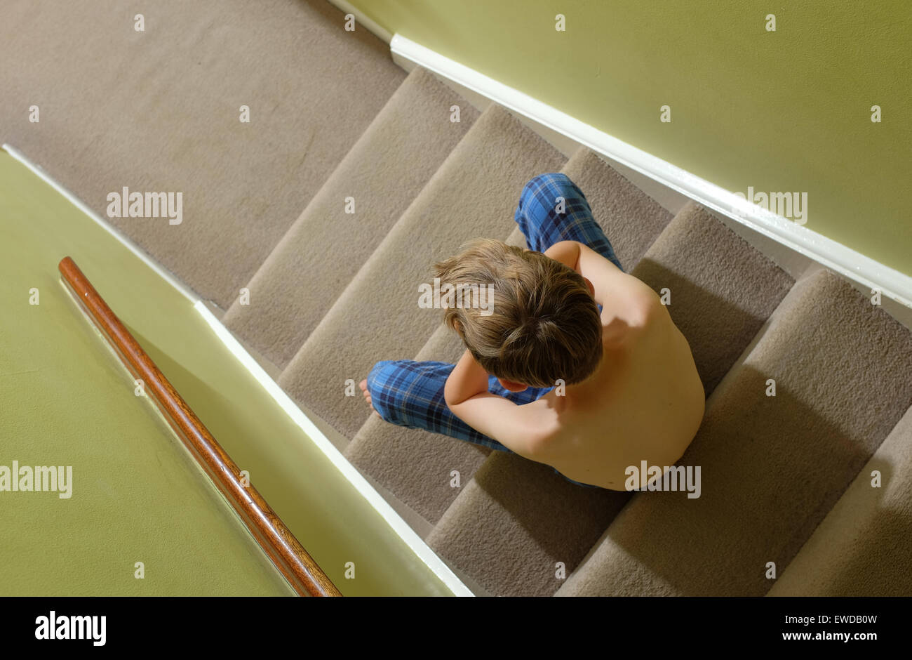 A child sitting on the stairs with his head in his hands looking upset Stock Photo