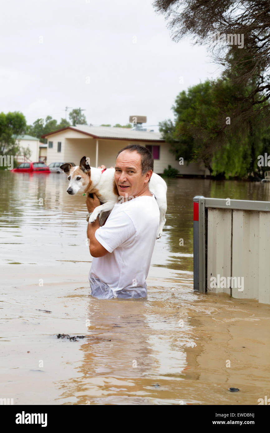 An older man saving his beloved dog during a flood and showing flooded items in the background. Stock Photo