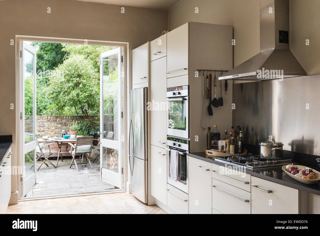 French windows open onto garden from kitchen area with stainless steel appliances and granite work surfaces Stock Photo
