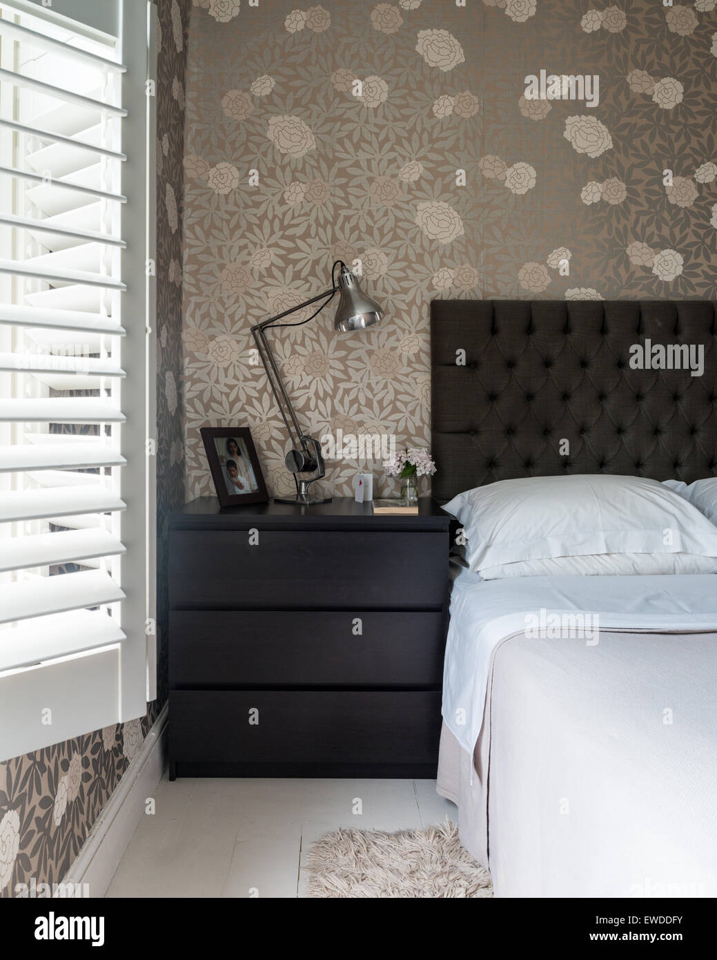 Osbourne & Little mettalic floral print wallpaper in bedroom with plantation shutters and buttoned headboard Stock Photo