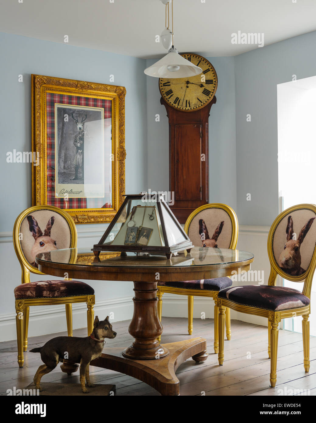 Three gilt dining chairs covered in Cory Visitorian hare head fabric round circular table in room with antique clock Stock Photo