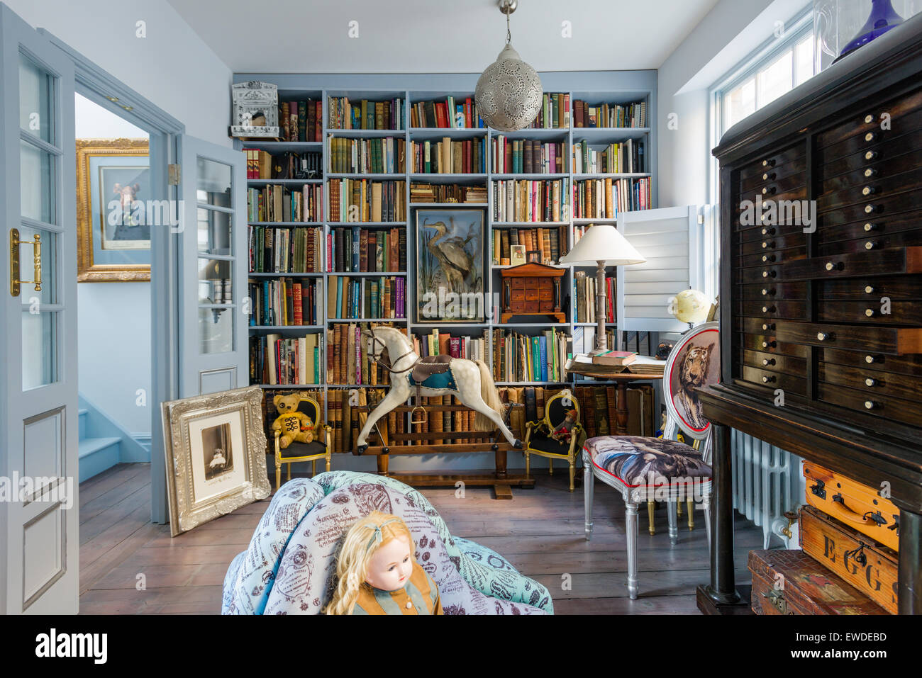 Blue painted shelves in library with antique rocking horse and Cory Visitorian upholstered chair Stock Photo