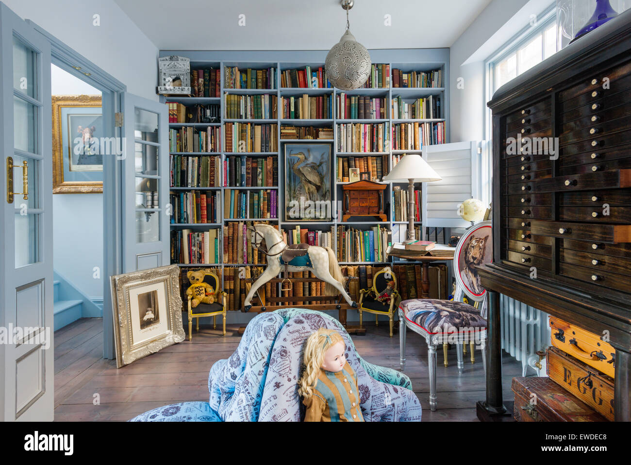 Blue painted shelves in library with antique rocking horse and Cory Visitorian upholstered chair Stock Photo