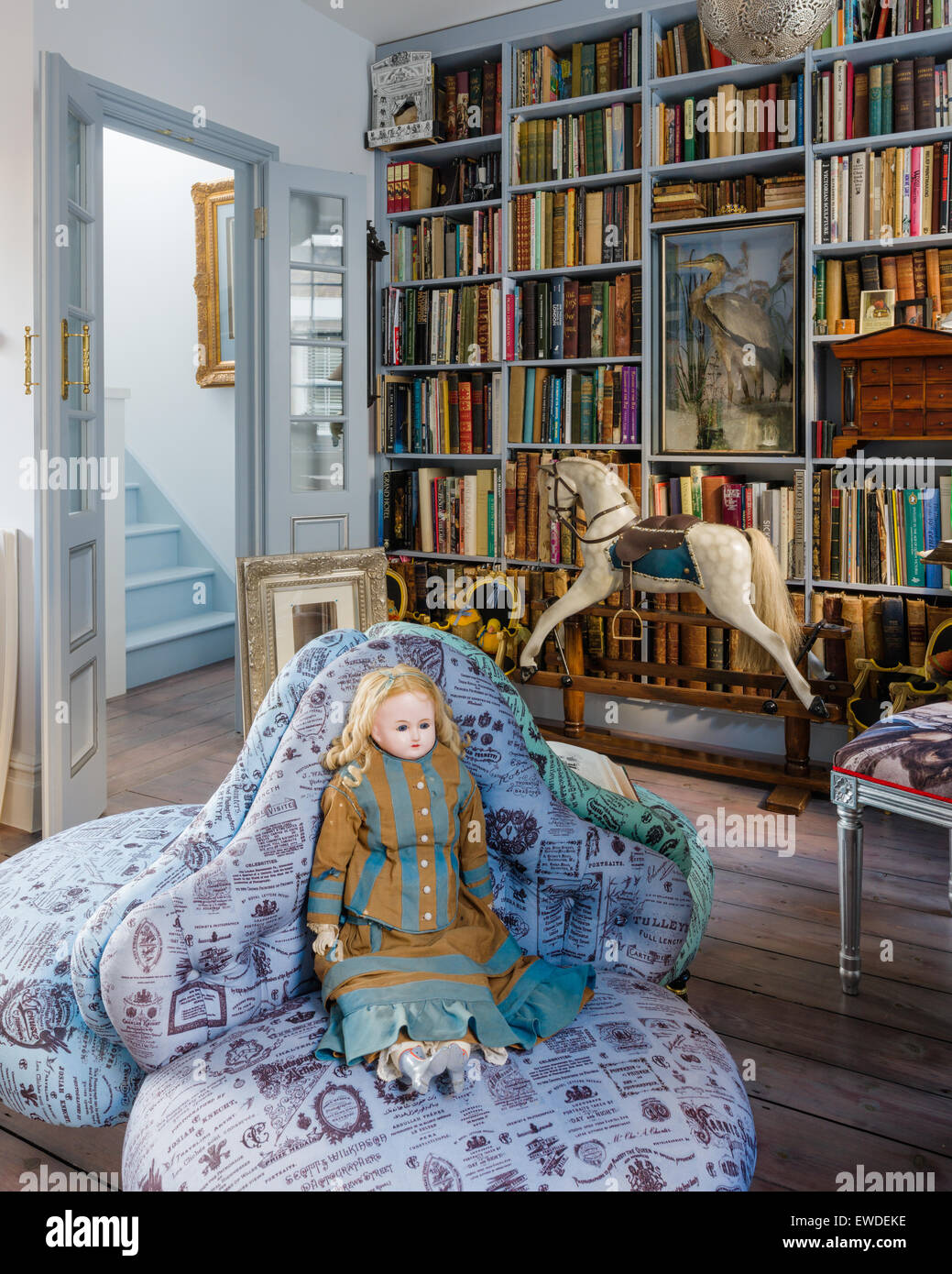 Antique doll on trio of buttoned Visitorian armchairs upholstered in Cory's visiting card fabric in library with antique rocking Stock Photo