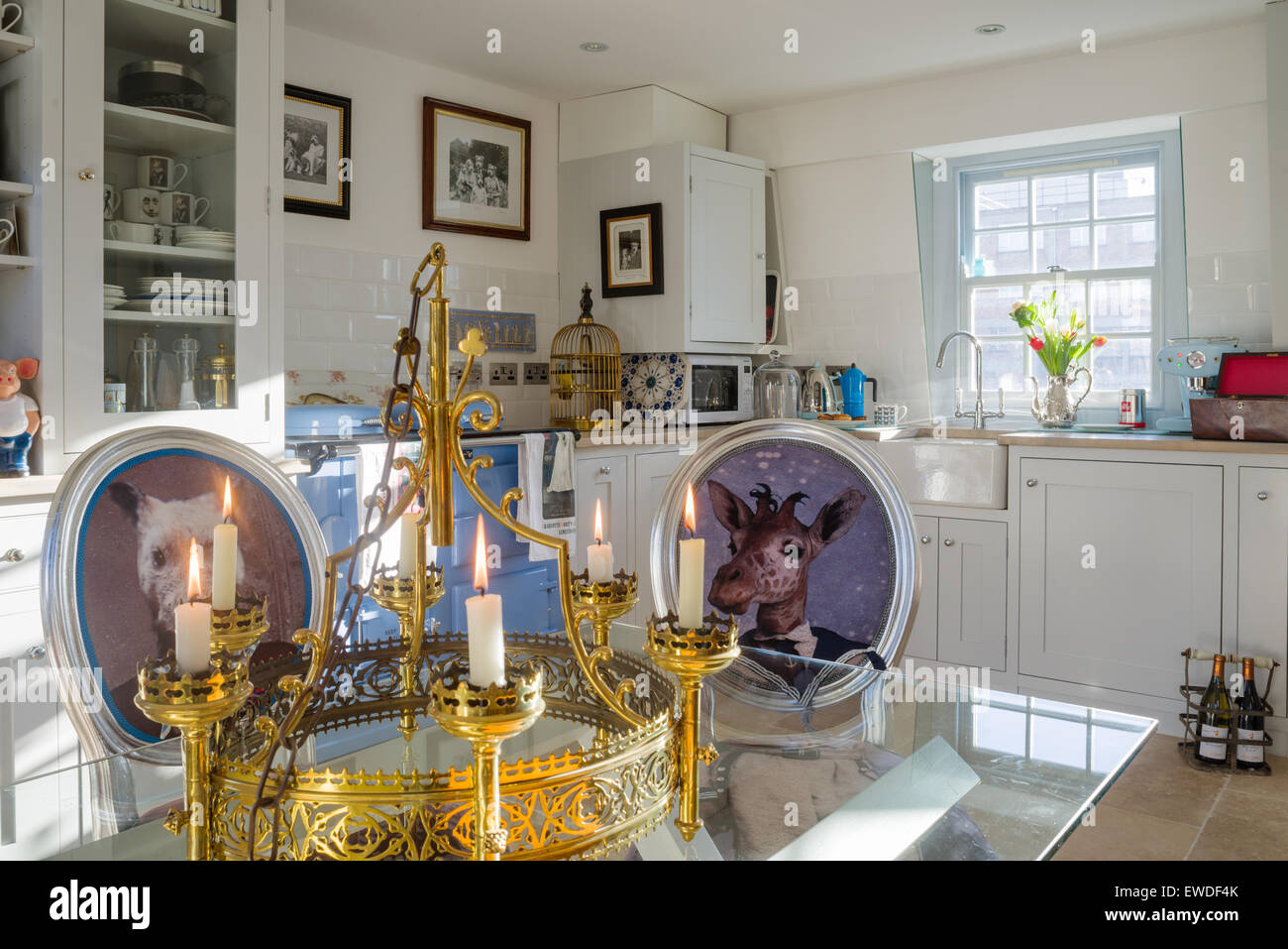Dining chairs upholstered in Cory's Visitorian prints around glass topped dining table in kitchen with white dresser and aga Stock Photo