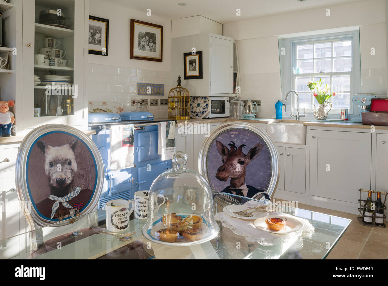Dining chairs upholstered in Cory's Visitorian prints around glass topped dining table in kitchen with white dresser and aga Stock Photo