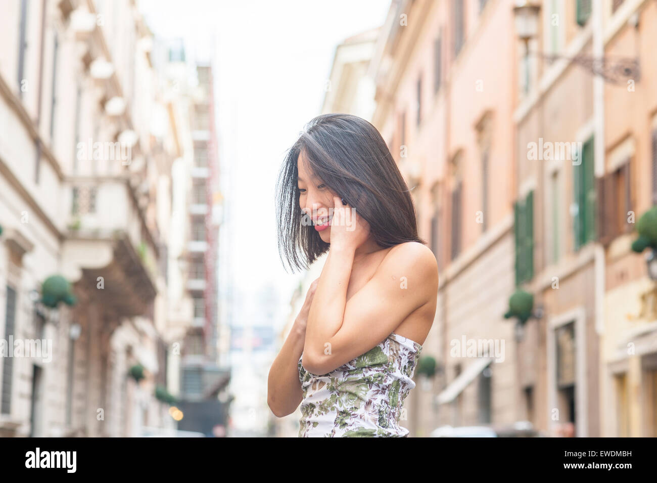 Young beautiful asian woman looking up smiling and talking using mobile phone urban outdoor spring dressing Stock Photo