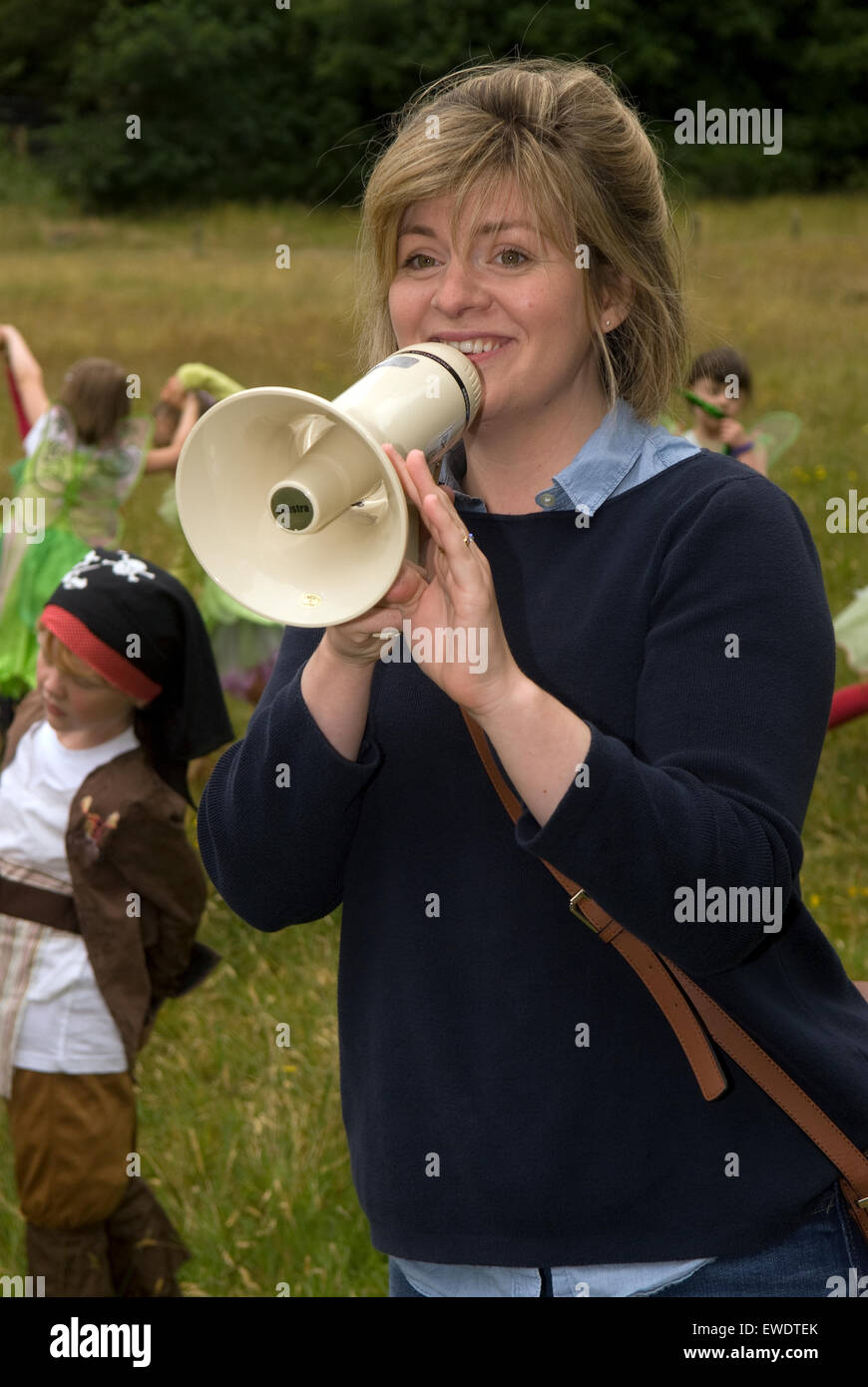 Young woman using megaphone to organise the crowds prior to a community summer parade, Frensham, Surrey, UK. Stock Photo