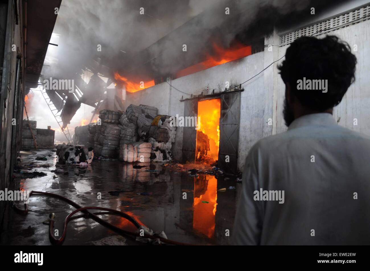 Karachi. 24th June, 2015. A man stands as a fire erupts at a warehouse