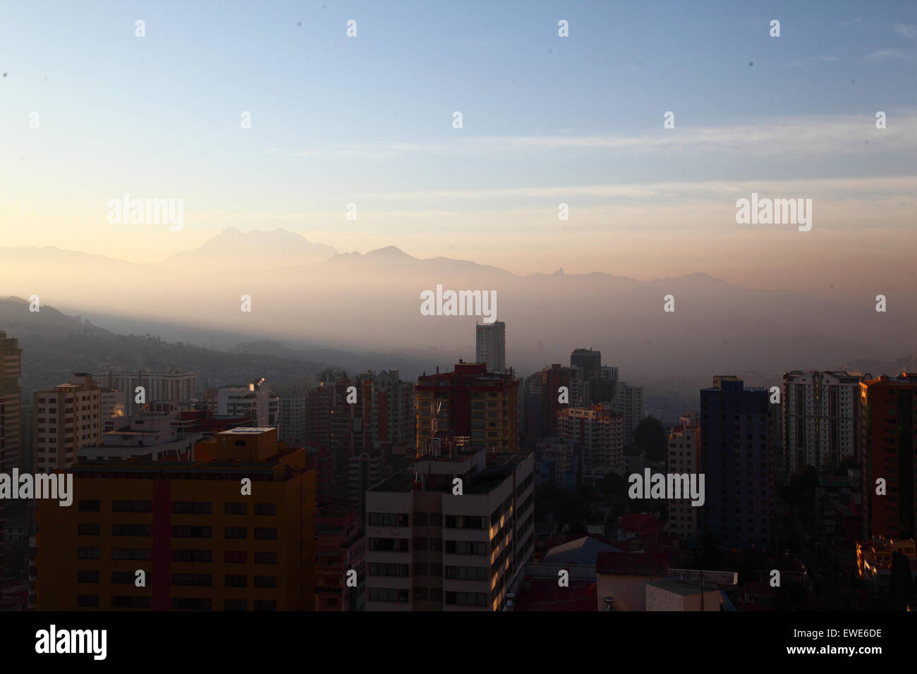 La Paz, Bolivia, 24th June 2015. Smoke fills the valleys of the lower part of La Paz shortly after sunrise after San Juan night. San Juan is traditionally believed to be the coldest part of the year and many people in Bolivia light bonfires and set off fireworks. Local authorities have been attempting to stop this custom in the last few years to reduce the extra pollution it causes in the city, but with only limited success. The peak in the background is the 6439m high Mt Illimani. Stock Photo
