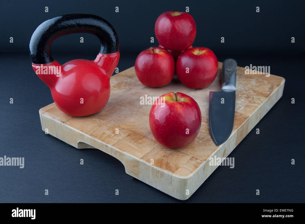 Red apples, knife, and kettlebell on chopping board Stock Photo