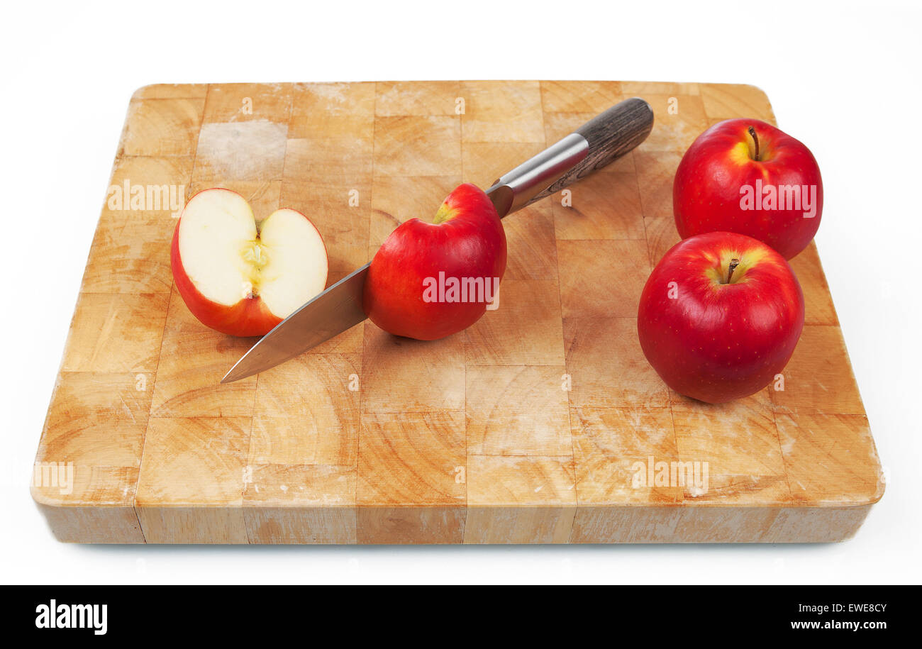 Knife cutting an apple on chopping board with two whole apples on the side. Stock Photo