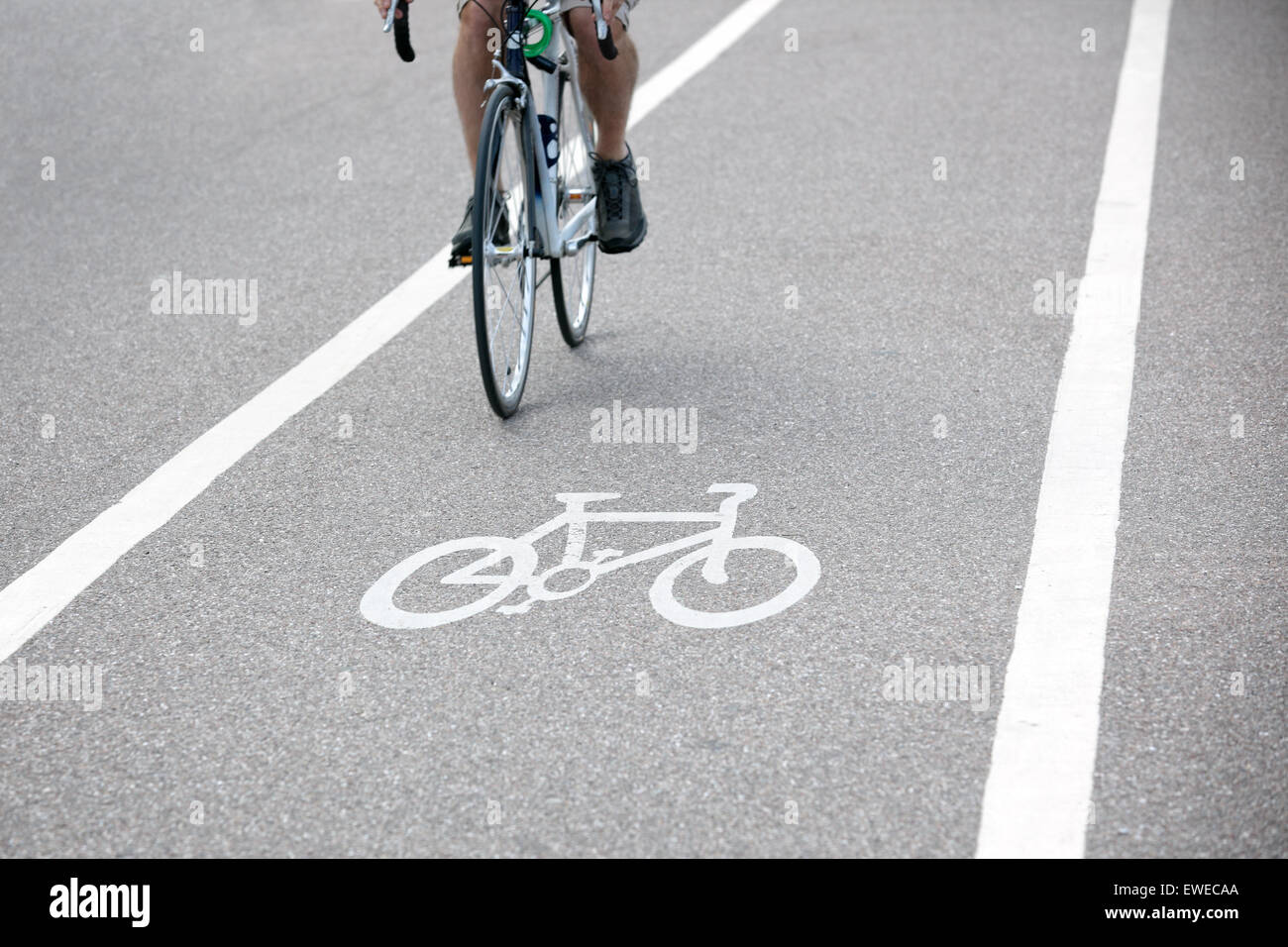 Commuter riding a bicycle on a city cycle lane or path across white painted bike symbol Stock Photo