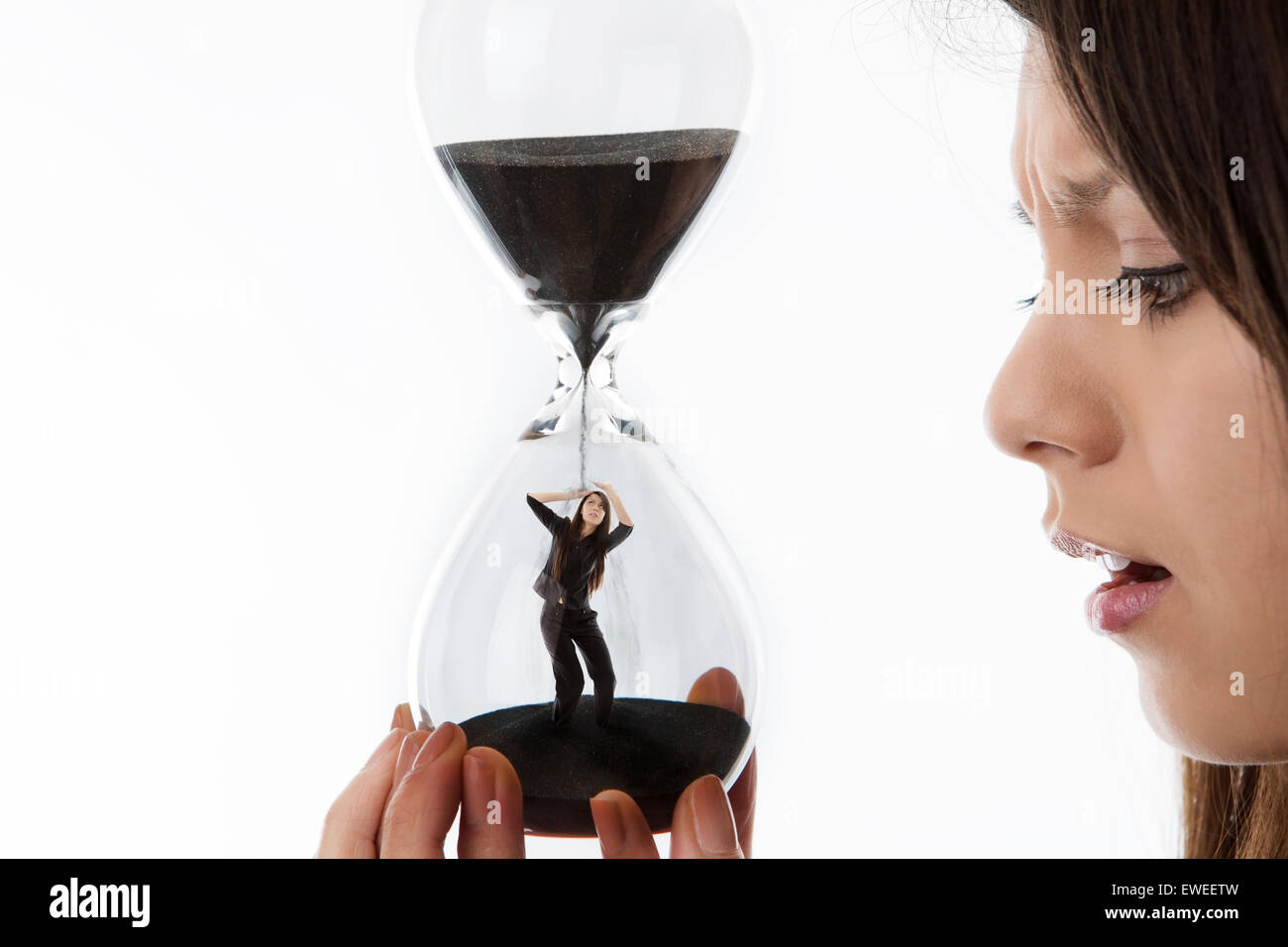 woman holding up a hour glass sand timer watching time slip away with herself inside the glass Stock Photo