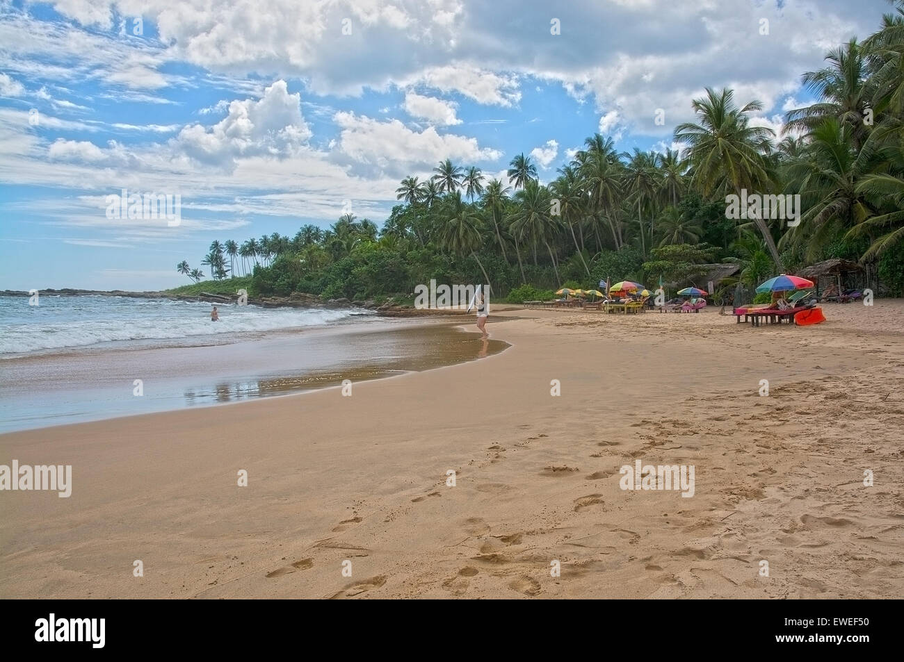 Beach with surfer woman and parasols on sandy beach in afternoon sun haze on the Rocky Point beach on December 21, 2015 in Tanga Stock Photo