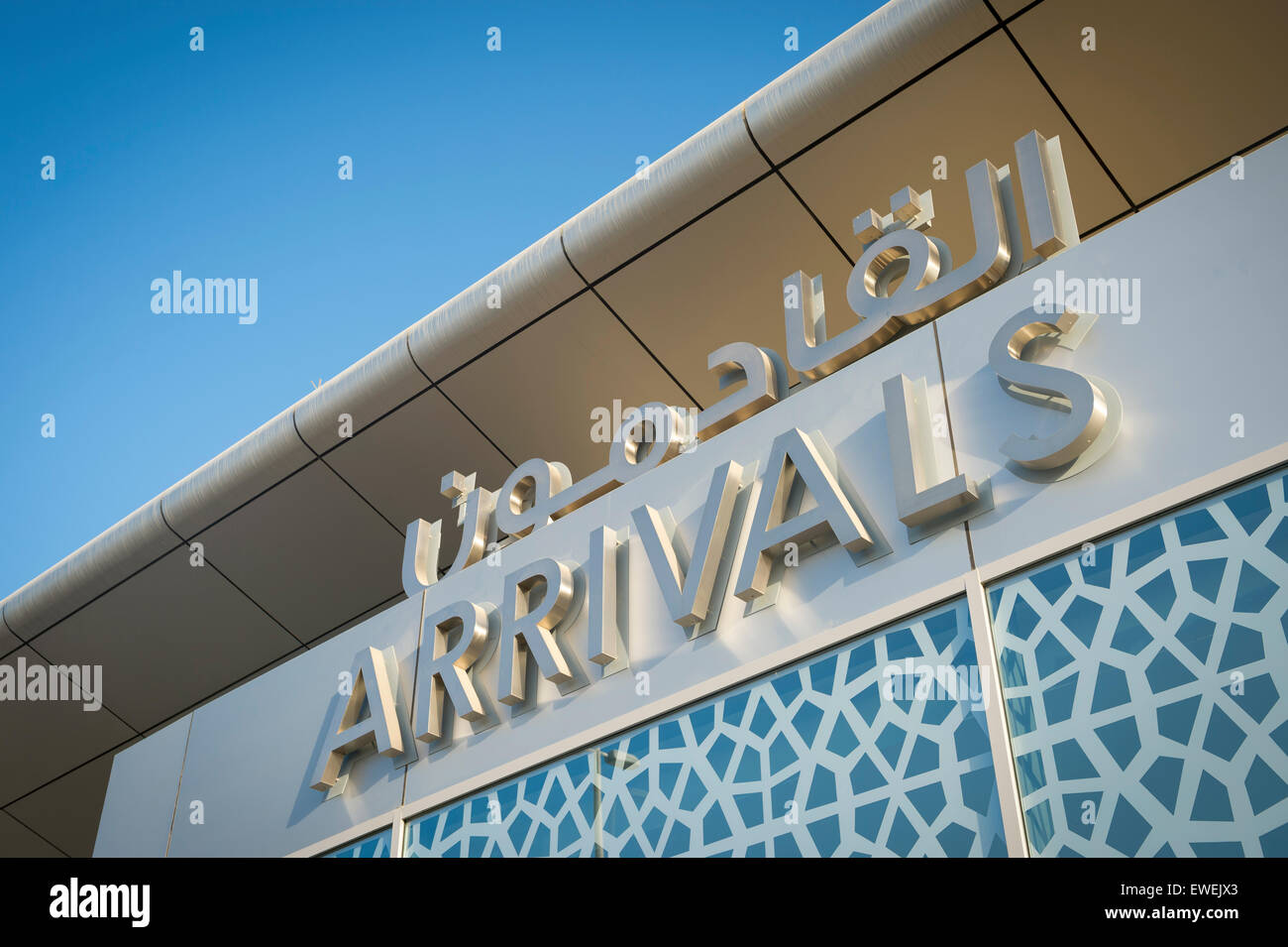 Arrivals sign at an airport in the Middle East features Arabic text and Islamic patterns under modern architecture and blue sky Stock Photo