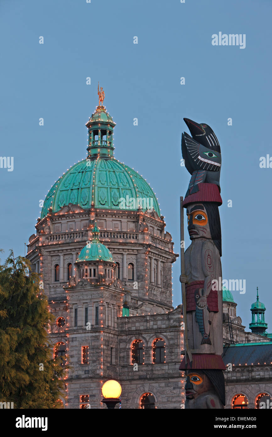 First Nations totem pole in front of the illuminated BC Parliament buildings in the Inner Harbour in the city of Victoria, Vanco Stock Photo