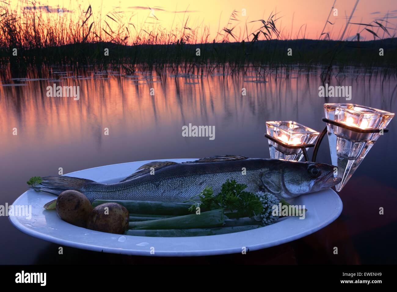 Fresh fish catch on a plate with vegetables above water by the lake at sunset time Stock Photo