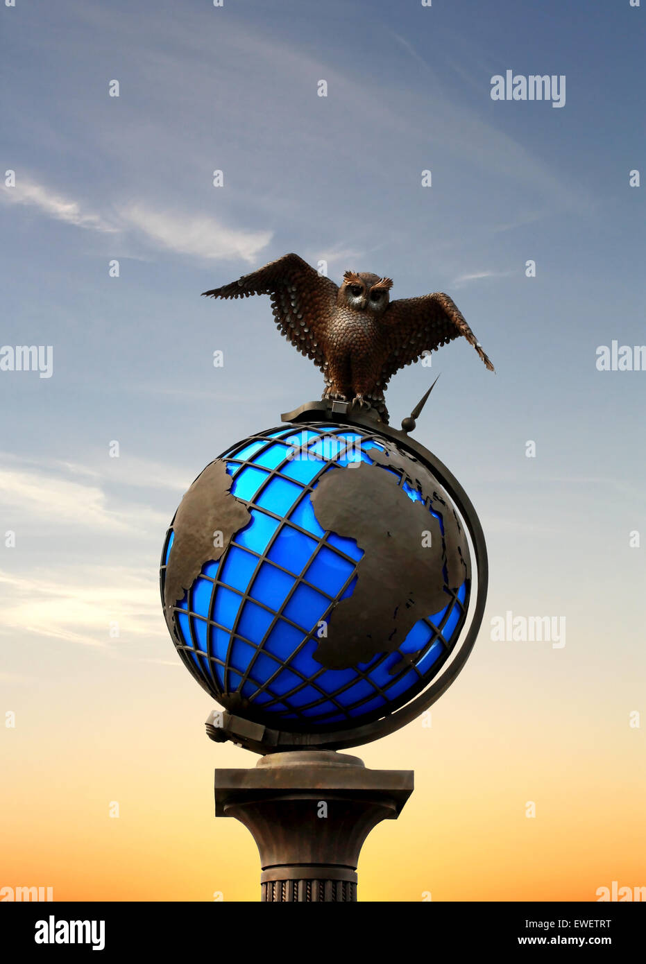 Bronze owl on a pedestal in a form of globe on the background of  sunset sky Stock Photo