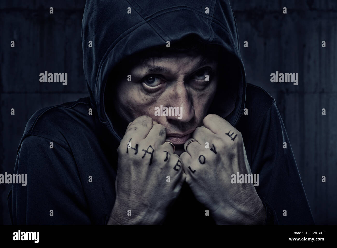 Grizzled man in hooded jacket with fists marked 'Hate' and 'Love' Stock Photo
