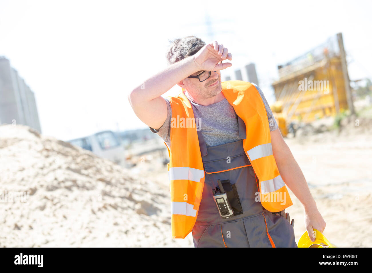 Tired construction worker wiping forehead at site Stock Photo