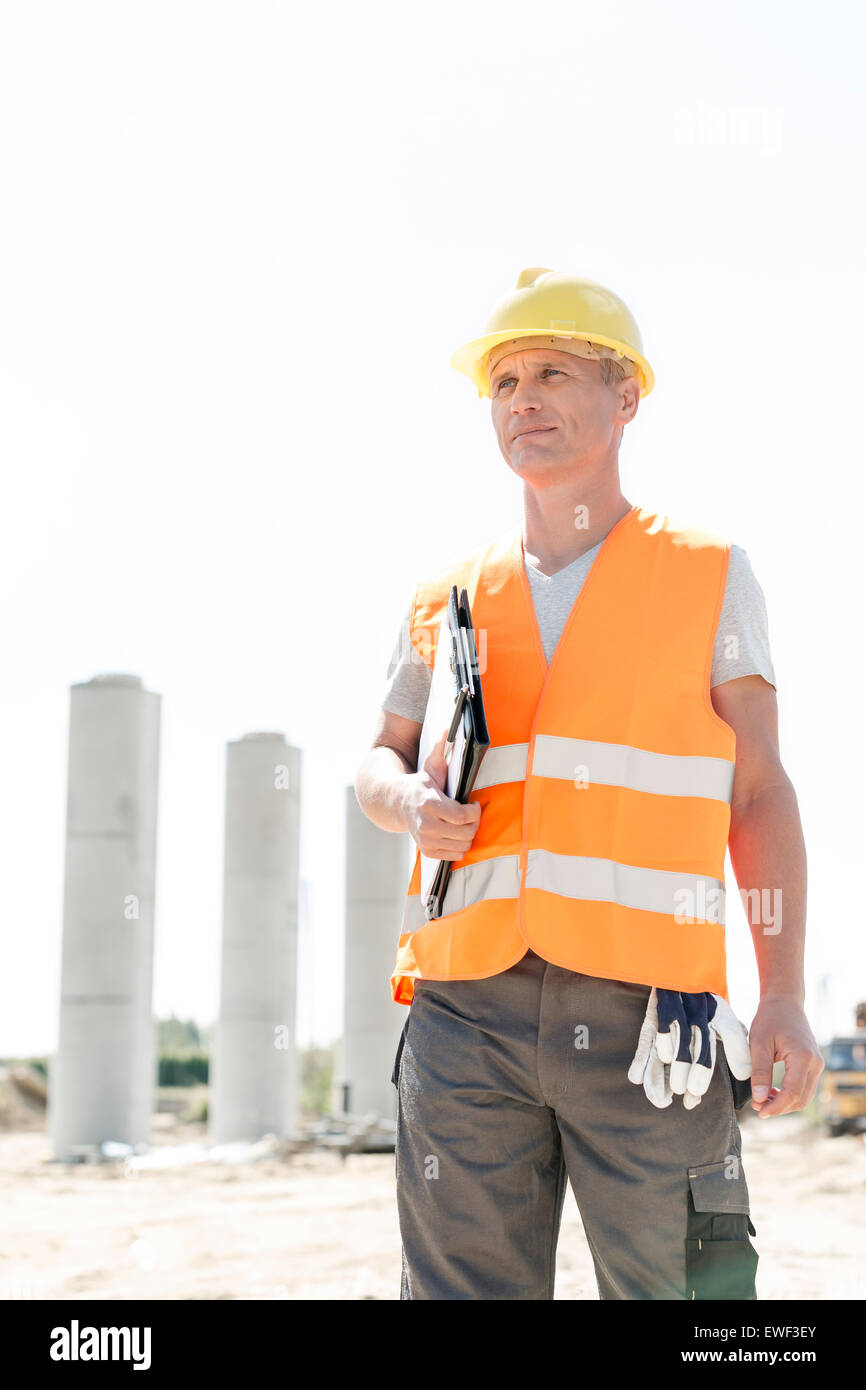 Thoughtful architect looking away while holding clipboard at construction site Stock Photo