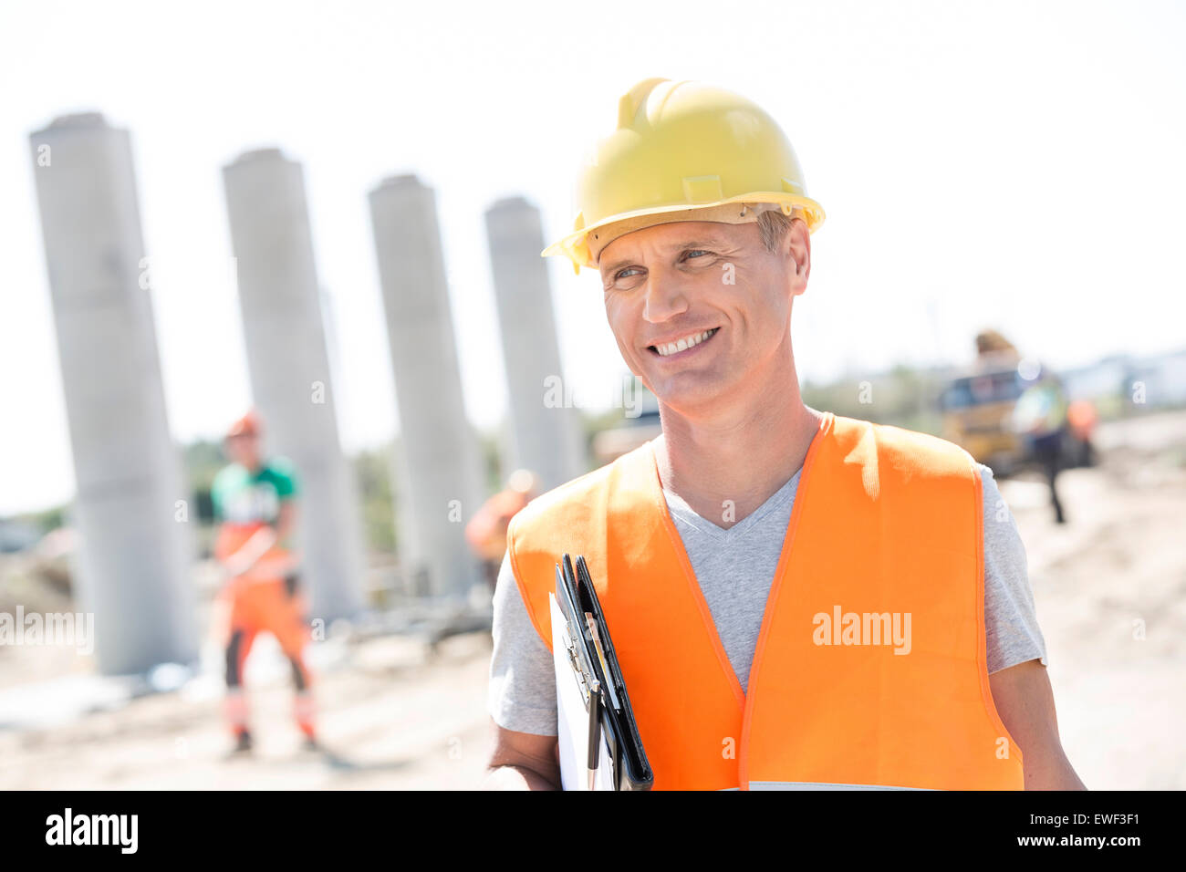 Happy architect looking away while holding clipboard at construction site Stock Photo