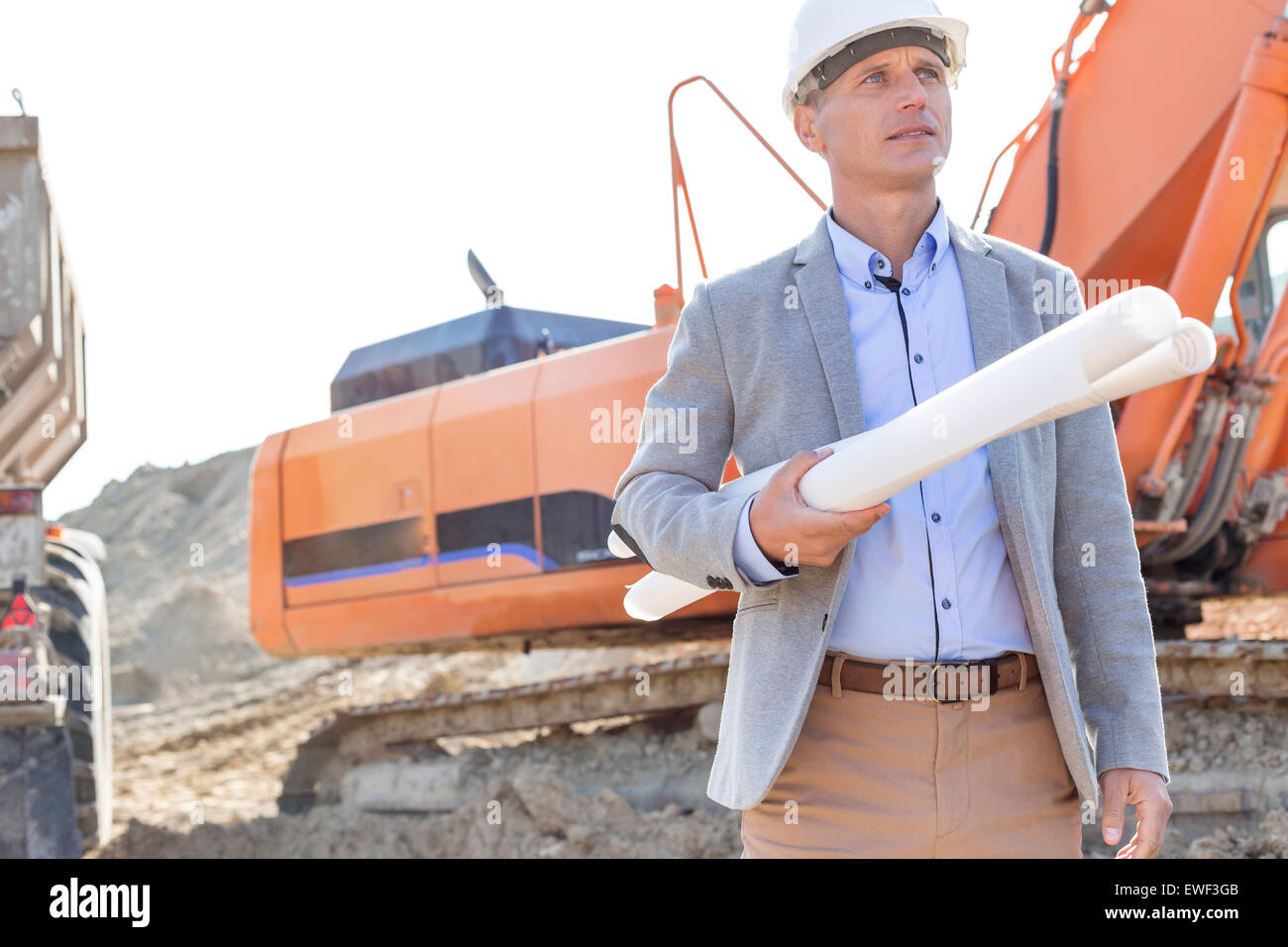 Confident architect looking away while holding blueprints at construction site Stock Photo