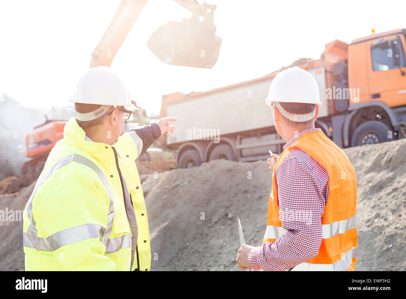 Engineer pointing at vehicles while discussing at construction site Stock Photo