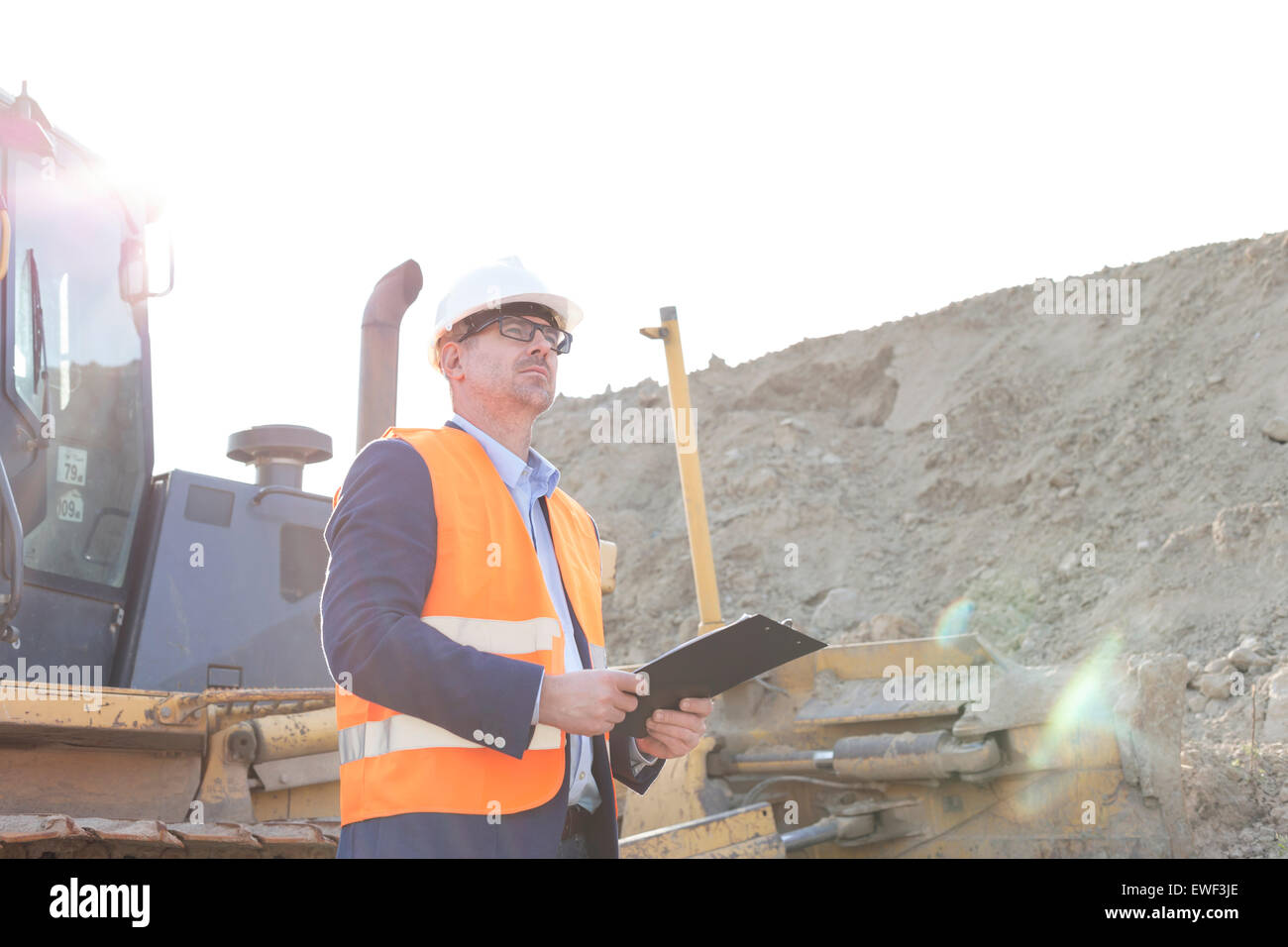 Engineer looking away while holding clipboard at construction site Stock Photo