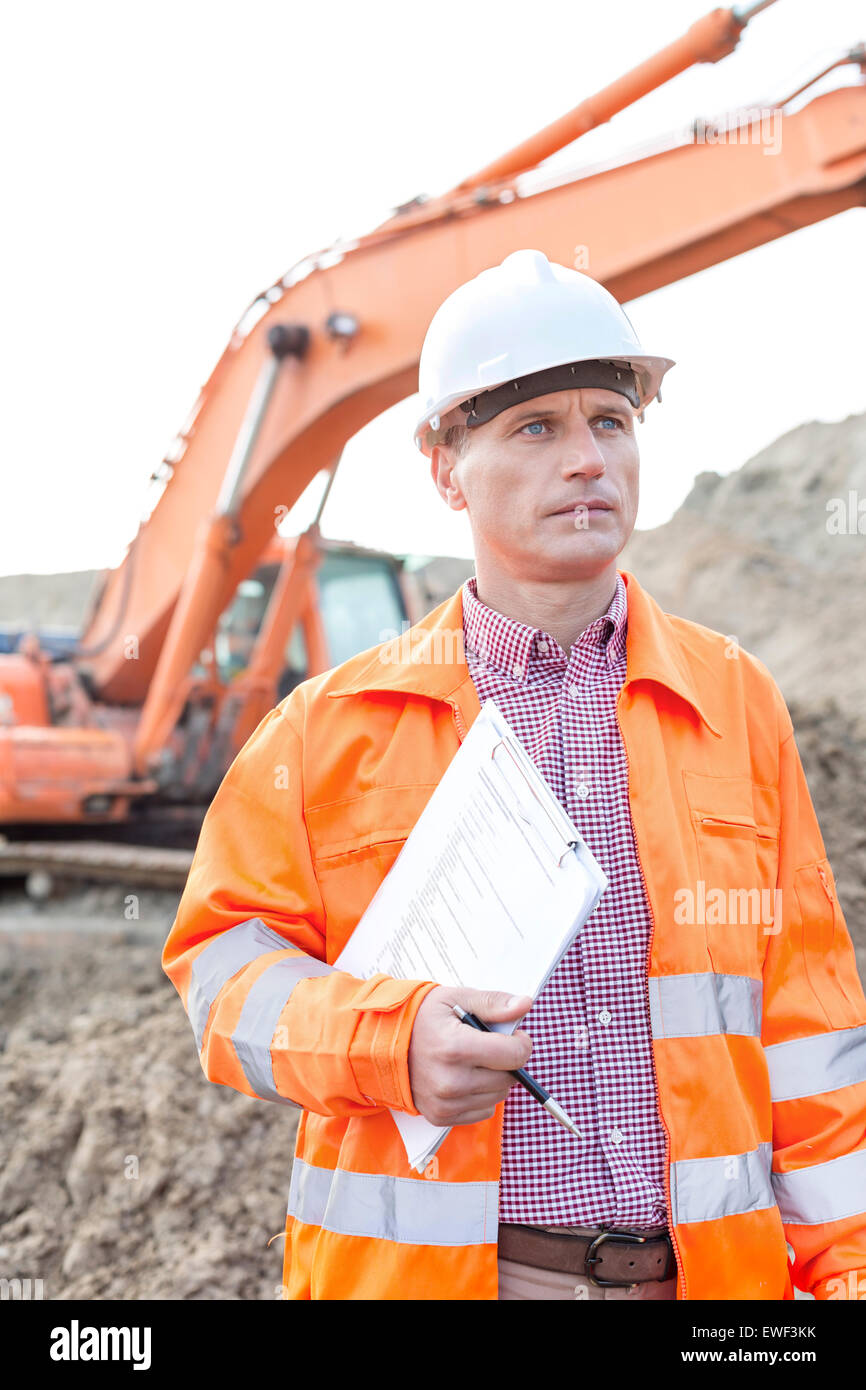 Architect looking away while holding clipboard at construction site Stock Photo