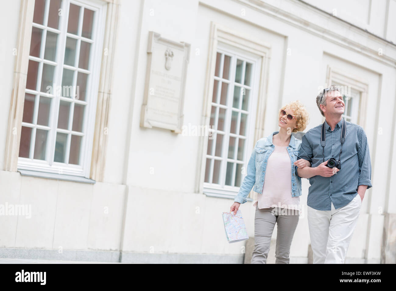 Happy middle-aged tourist couple walking arm in arm by building Stock Photo