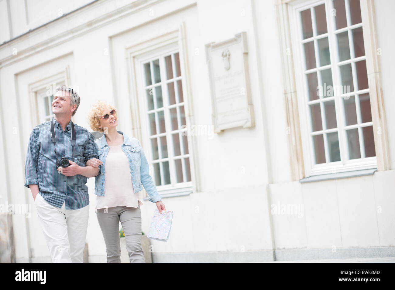 Happy middle-aged tourist couple walking arm in arm by building Stock Photo