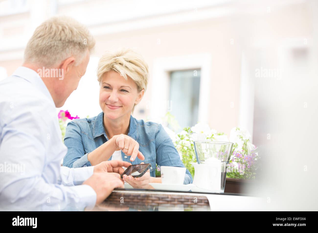 Happy middle-aged couple using cell phone at sidewalk cafe Stock Photo