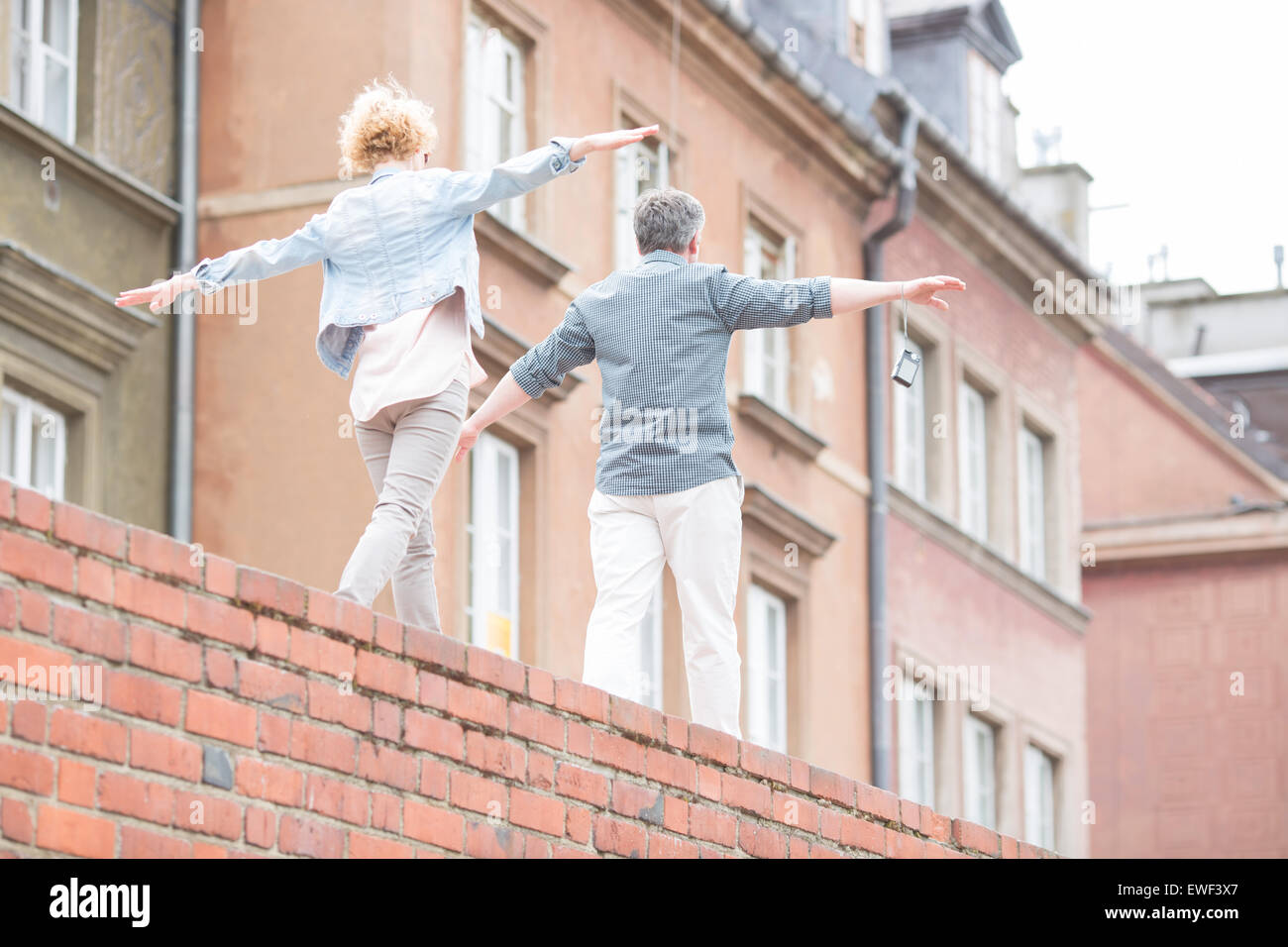 Rear view of middle-aged couple with arms outstretched walking on brick wall Stock Photo
