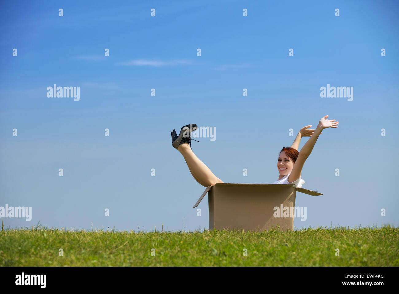 Cheerful young woman sitting in cardboard box at park with arms Stock ...
