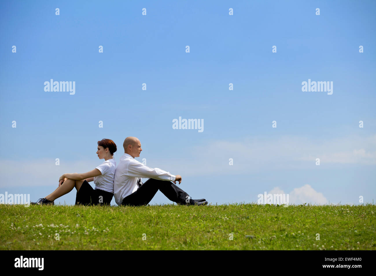 Business couple sitting back to back on grass Stock Photo