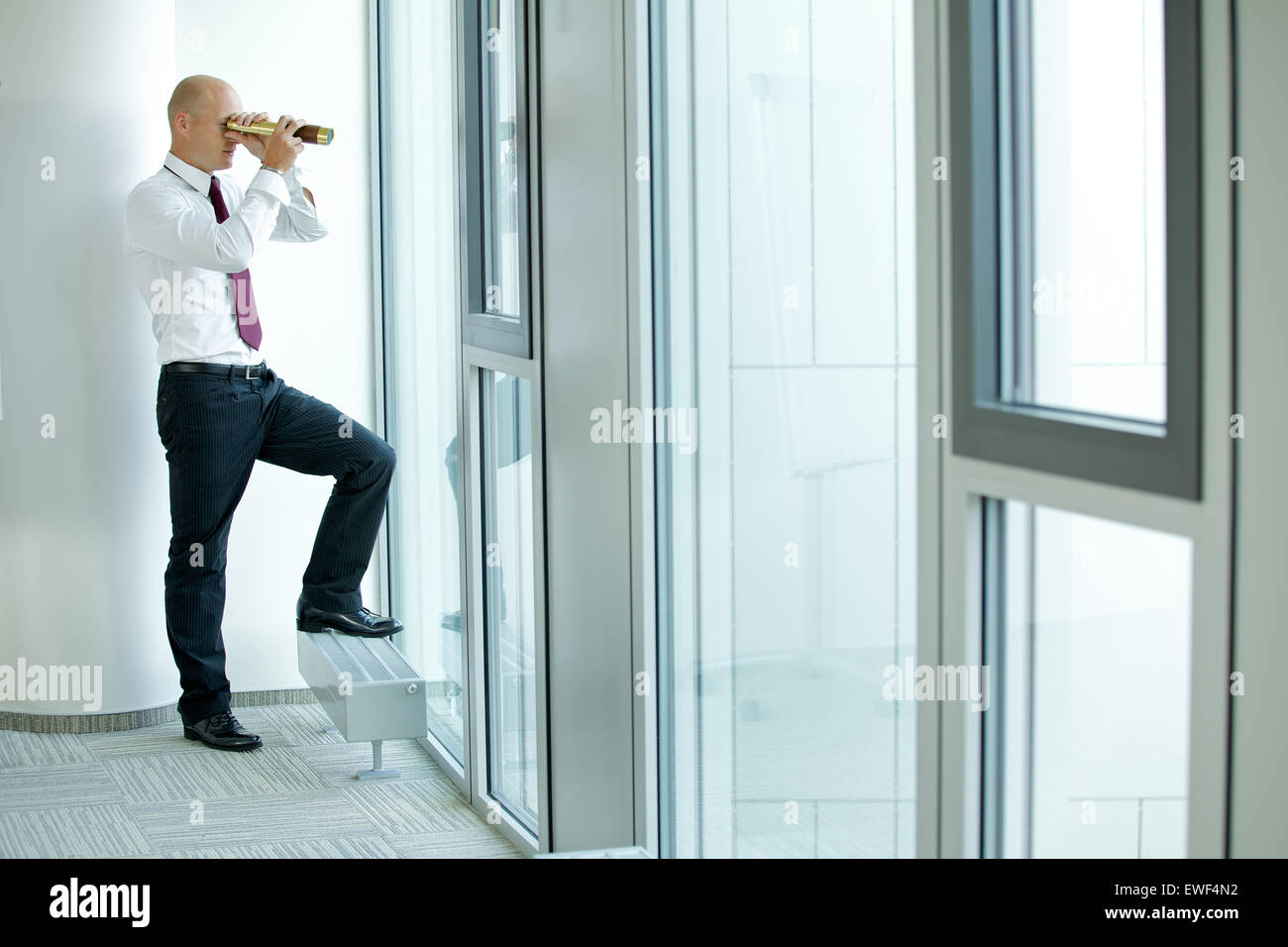 caucasian businessman spying using telescope thru office window Stock Photo