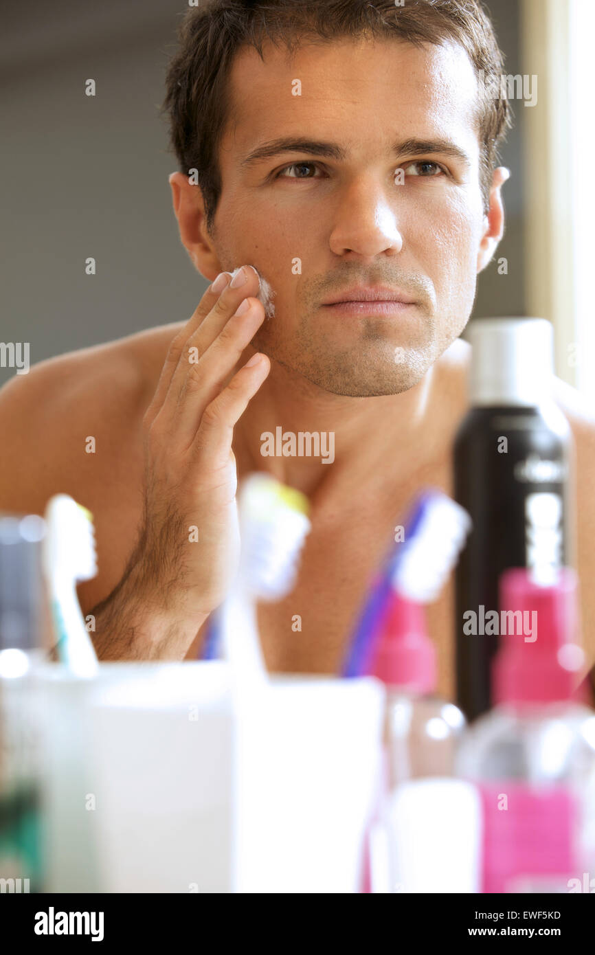 Reflection of young man in mirror applying shaving cream Stock Photo