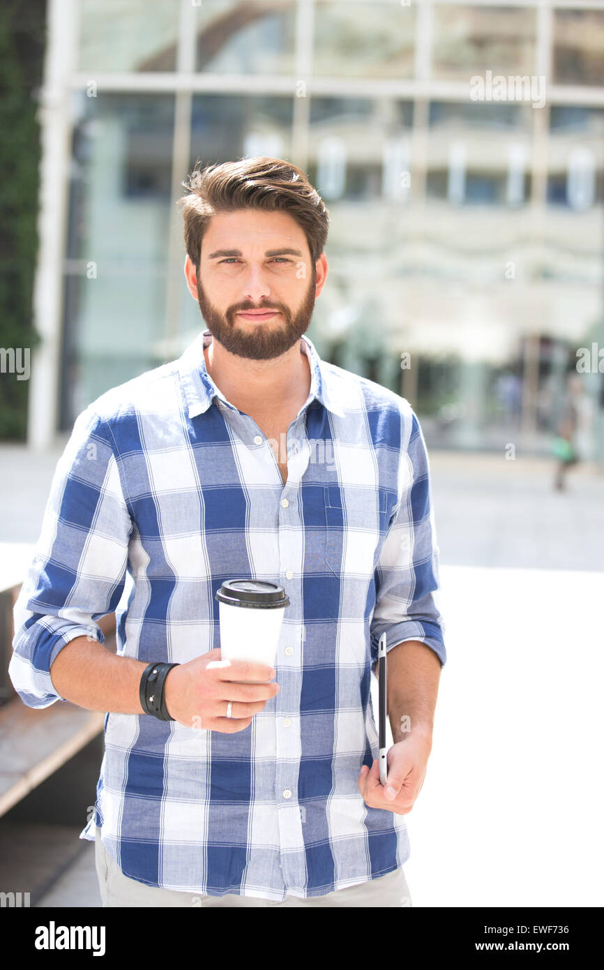 Portrait of confident man looking away while holding disposable cup and tablet PC in city Stock Photo