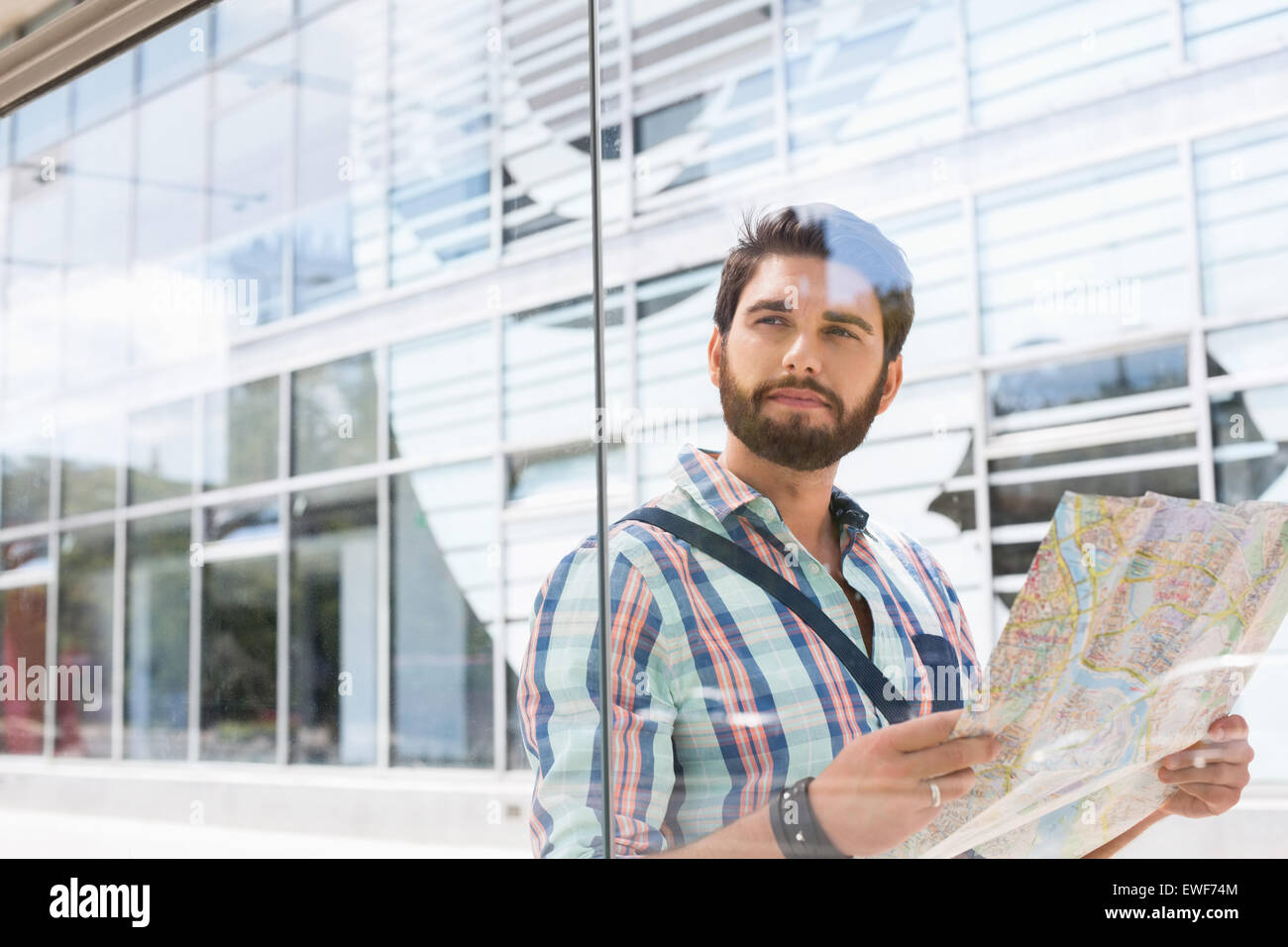 Thoughtful man looking away while holding road map against glass wall Stock Photo