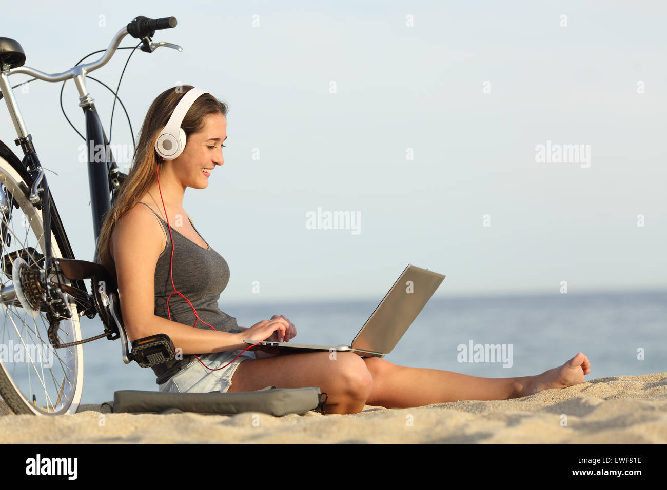 Teen girl studying with a laptop on the beach leaning on a bicycle Stock Photo