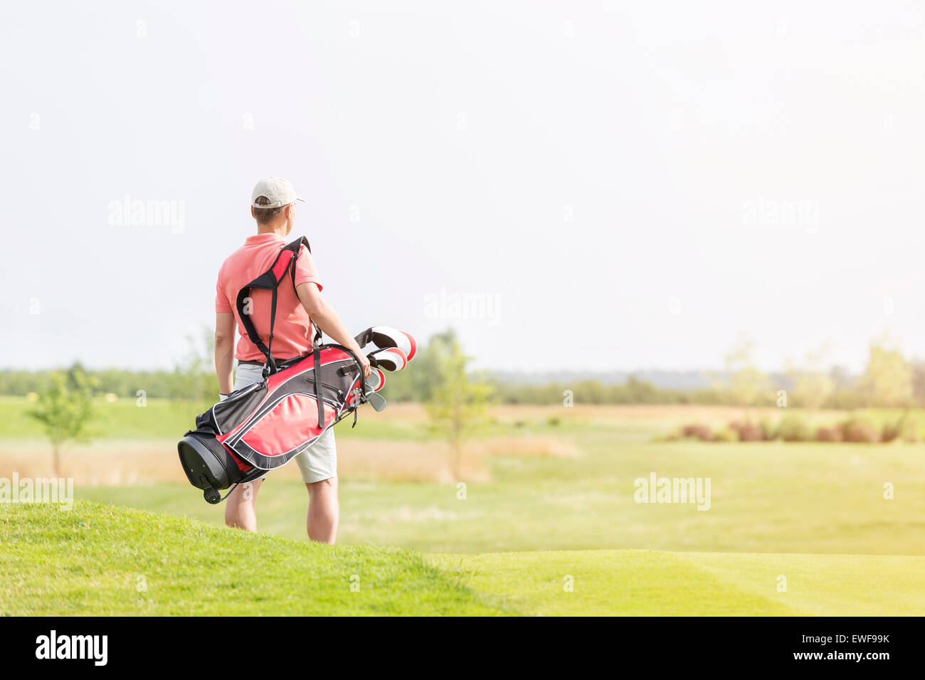 Rear view of man carrying golf club bag while walking at course Stock